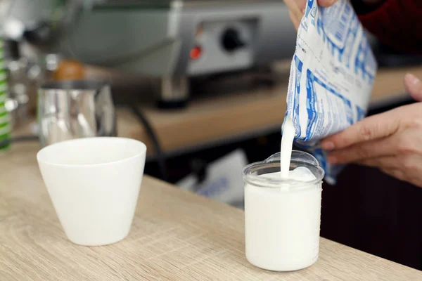 Barista sur une table de bar en bois dans un café verse du lait dans du verre pour préparer le latte — Photo