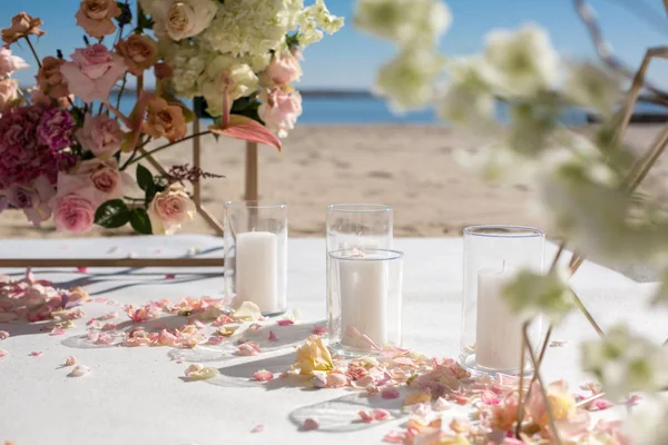 Fresh flower petals lie on the floor next to a decorated wedding arch and white candles. Event decoration with fresh flowers