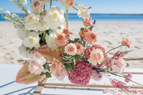 Part of the wedding arch decorated with fresh flowers is set on the sandy bank of the river. Wedding florist arranges workflow — Stock Photo, Image