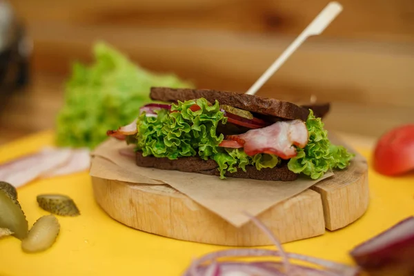 Grilled dark bread sandwich on wooden plate on yellow board — Stock Photo, Image