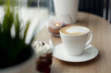 Beyaz fincan beyaz daire üzerinde sıcak cappuccino ve ahşap bar masa pencere yanında kırmızı kadife tatlı. Dışarıda soğuk karlı havalarda