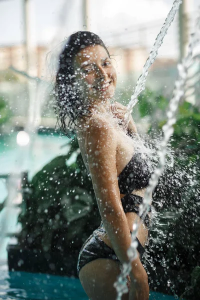 Sexy hembra delgada en traje de baño toma ducha en la piscina entre arbustos verdes en la azotea con fondo de paisaje urbano Vacaciones de lujo en Asia . —  Fotos de Stock