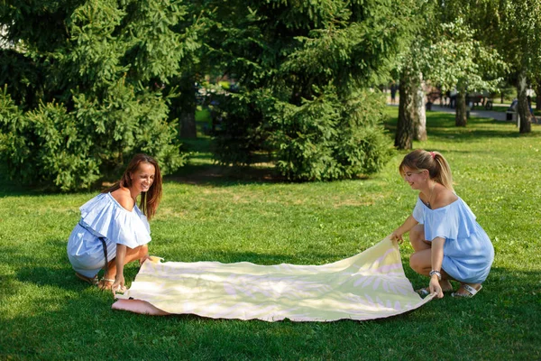 緑の牧草地に 2 人の女の子は、ピクニック毛布を広げた。夏の週末 — ストック写真
