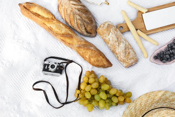 Food lay out on picnic blanket. fresh baked bread, grapes, olives and photocam lay on white blanket. Picnic prepare decoration