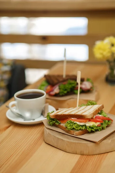 Φρέσκα ζουμερά σάντουιτς με φλιτζάνι ζεστό καφέ σε ξύλινο τραπέζι με — Φωτογραφία Αρχείου