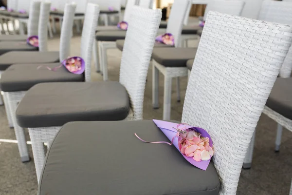 Фиолетовый мешок с розовыми лепестками роз, которые будут посыпаны на молодоженов лежал на стуле для гостей свадебной церемонии. Украшение мероприятия свежими цветами — стоковое фото