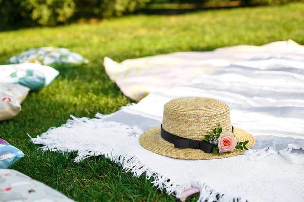緑の芝生の明るい夏の日の背景に白のピクニック毛布の上に新鮮な花をあしらったストロー ハットが横たわっていた。夏の週末のレジャー — ストック写真