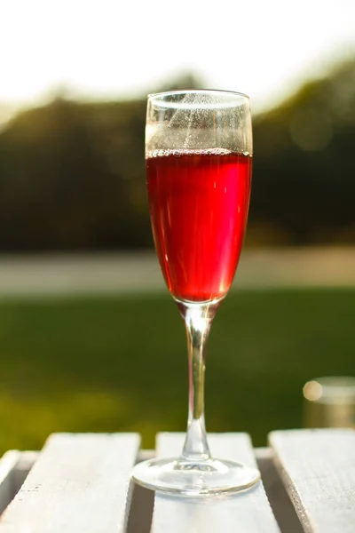 Verre à vin avec porte-champagne rouge sur une table en bois au fond vert du parc d'été — Photo