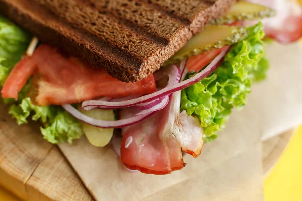 Closeup juicy sandwich with grilled dark bread and bacon — Stock Photo, Image