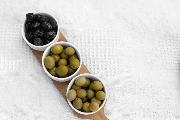 Set of three white bowls with olives on wooden tray on white blanket — Stock Photo, Image