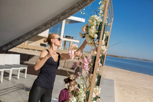 Florist girl decorates wedding arch with fresh flowers on the sa