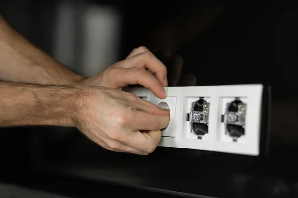 Close-up of an electrician\'s hand without any tools and gloves disassembling a white electrical outlet on a black glass wall