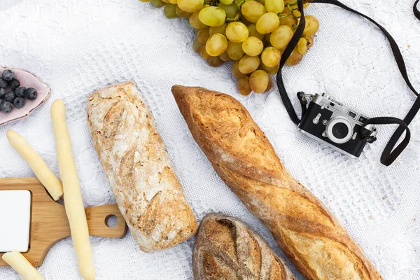 Food lay out on picnic blanket. fresh baked bread, grapes, olives and photocam lay on white blanket. Picnic prepare decoration