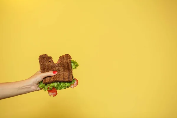 As mãos da mulher seguram sanduíche mordida no fundo amarelo. Conceito de promoção de sanduíches — Fotografia de Stock