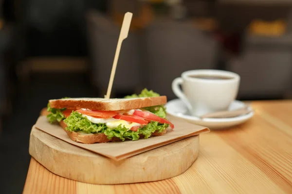 Свіжий соковитий бутерброд з чашкою гарячої кави на дерев'яному столі з темним фоном — стокове фото