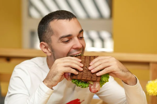 Jovem faminto em resaurante comer sanduíche — Fotografia de Stock