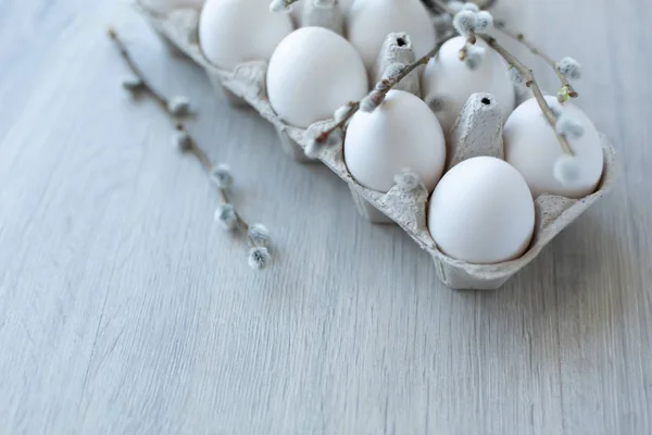 White chicken eggs in an open cardboard box on a light background decorated with willow branches with soft white buds. A dozen eggs in eco-friendly packaging. Healthy organic food and diet concept. Ea Stock Photo