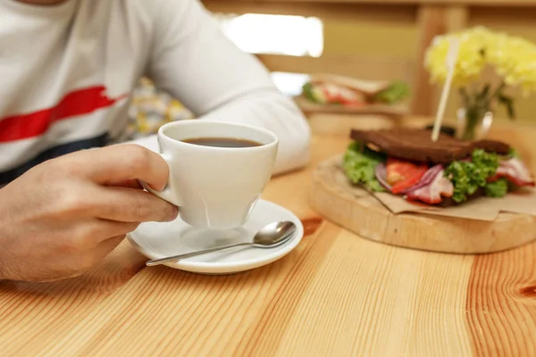 남자 잡아 샌드위치 배경에서 커피의 흰색 컵 — 스톡 사진