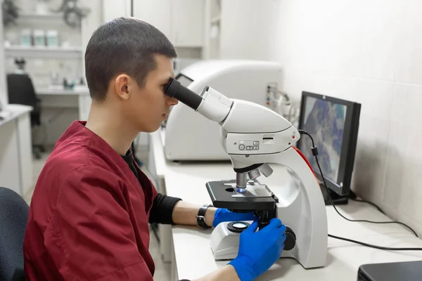 若い科学者が研究室で顕微鏡をのぞいてします。Yo — ストック写真