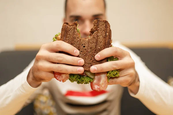 Closeup engraçado desfocado protrait de jovem segurar sanduíche mordido — Fotografia de Stock