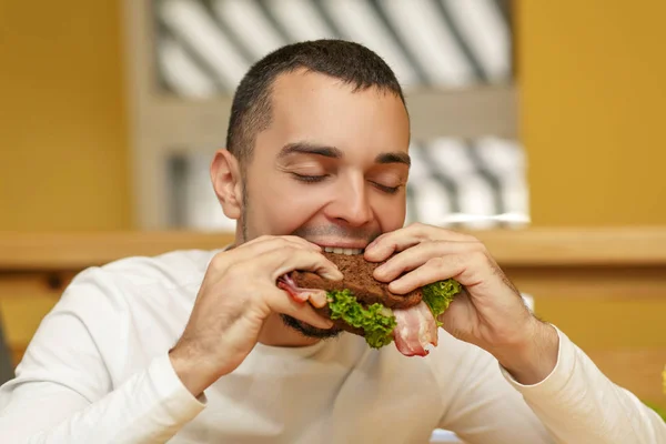 Hungry young man in resaurant eat sandwich — Stock Photo, Image
