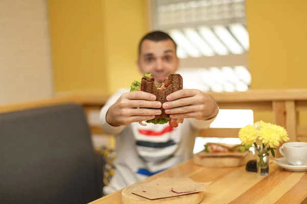 Nahaufnahme lustig verschwommene Länge des jungen Mannes halten gebissenes Sandwich — Stockfoto