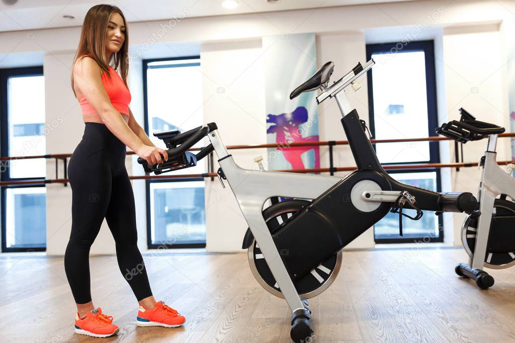 Portrait young slim woman in sportwear posing at exercise bike i