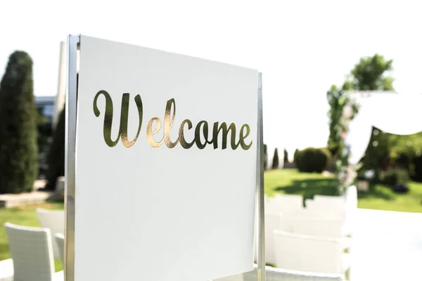 Hermosa boda extrovertida. Romántica ceremonia de boda, boda al aire libre en el césped vista al agua. Decoración de la boda. Sillas de madera blanca en un césped verde. Sillones blancos para invitados. Señal de bienvenida —  Fotos de Stock