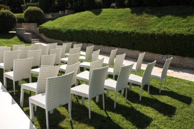 Güzel bir düğün hazırlığı. Romantik bir düğün töreni. Çimenli su manzaralı bir düğün. Düğün dekoru. Yeşil çimenlikteki beyaz tahta sandalyeler. Misafirler için beyaz koltuklar