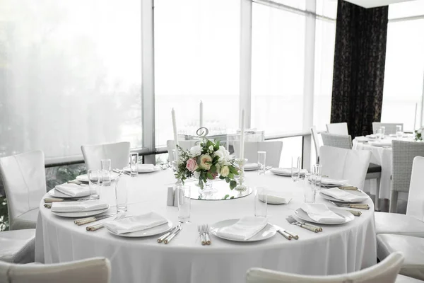 Обстановка весільного столу прикрашена живими квітами. Білі тарілки, посуд, біла скатертина та біла кімната. Весільна флористика. Банкетний стіл для гостей. Букет з трояндами, гортензією та еустомою — стокове фото