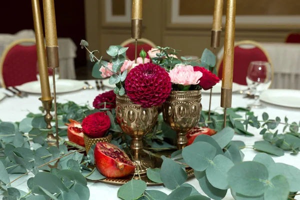 Bröllops bordet inställningen är dekorerad med färska blommor i en mässing skål och gyllene ljus i mässing ljus stakar. Bröllop blomster handlare. Bankettbord för gäster. Bukett med dahlior och eukalyptus — Stockfoto