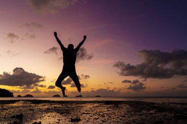 Gün batımında sahilde bir adamın silueti. İnsanoğlu gün batımına sevinir.