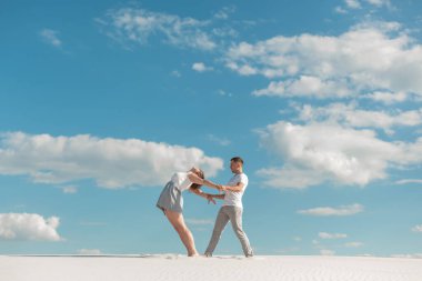 Romantik çift mavi gökyüzü arka planında kum çölünde dans ediyor.