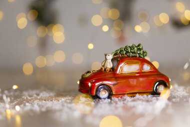 Noel temasının dekoratif figürleri. Bir oyuncak ayının oturduğu kırmızı bir arabanın heykeli. Noel ağacı süslemesi. Şenlikli dekor, sıcak bokeh ışıkları