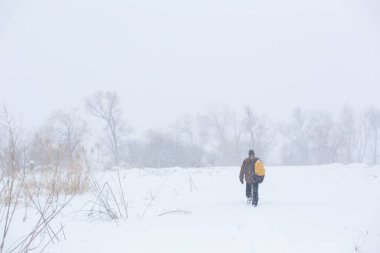 Kırsal bir adam kışın sarı bir sırt çantasıyla sokakta yürüyor. Kar fırtınası.