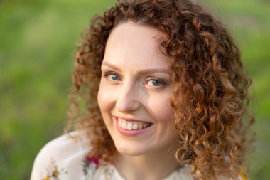 Yeşil çiçekli bahar parkında kıvırcık saçlı, gülümseyen çekici bir kadının yakın portresi. Saf duygular.