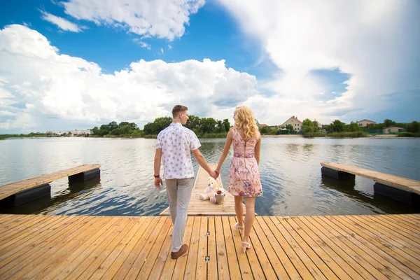 ロマンチックなデートの驚き 桟橋で湖を見下ろす若い男と少女 男は女の子にテディベアを与えます — ストック写真