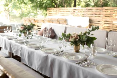 Pirinç bir vazoda taze çiçeklerle süslenmiş düğün masası. Düğün çiçekçisi olarak. Dışarıdaki yeşil manzaralı misafirler için bir ziyafet masası. Güllü buket, Eustoma ve okaliptüs yapraklı..