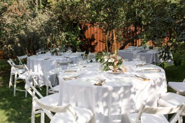 Pirinç bir vazoda taze çiçeklerle süslenmiş düğün masası. Düğün çiçekçisi olarak. Dışarıdaki yeşil manzaralı misafirler için bir ziyafet masası. Güllü buket, Eustoma ve okaliptüs yapraklı..