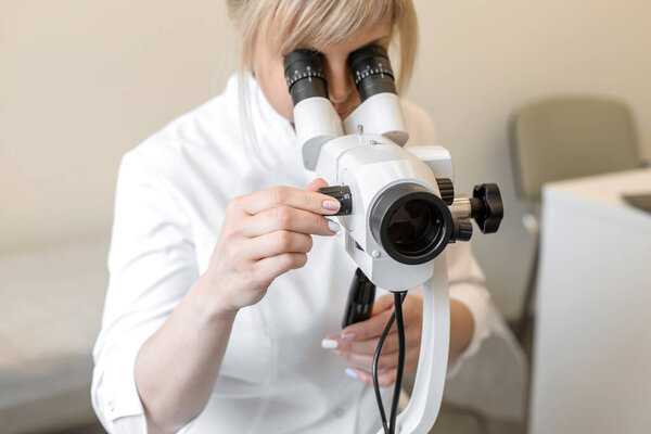 Female blond doctor gynecologist looks through a colposcope. Examination by a gynecologist. Female health concept.