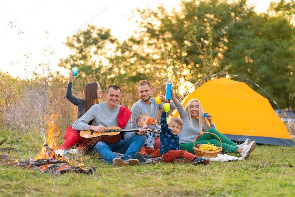 travel, tourism, hike, picnic and people concept - group of happy friends with tent and drinks playing guitar at camping.