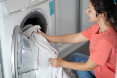 Kirli çamaşırları bir dairede yerde otururken çamaşır makinesine atan bir kız. Çamaşır günü, ev işi..