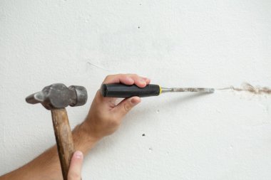 Binanın tamiri. Bir adam duvara kablo döşemek için hendek kazar. Duvara elektrik kabloları döşeniyor.