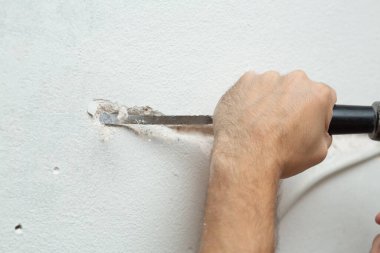 Binanın tamiri. Bir adam duvara kablo döşemek için hendek kazar. Duvara elektrik kabloları döşeniyor.
