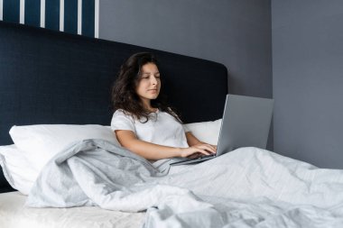 Yatakta dizüstü bilgisayarlı güzel esmer kız. Sabahtan akşama kadar çalış. Elektronik aletler yatmadan önce ya da sabah