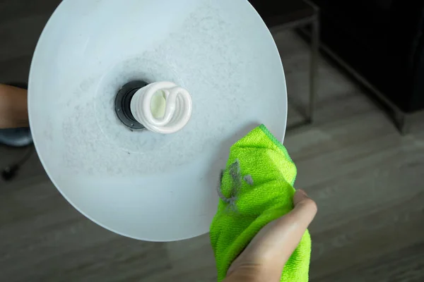 Cleaning the house. Wipe off the dust with a green rag from the floor lamp. Energy saving light bulb. A lot of dust