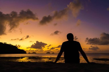 Bir erkek silueti tropik bir plajda güzel bir günbatımının tadını çıkarır. Okyanusta yakıcı gün batımı.