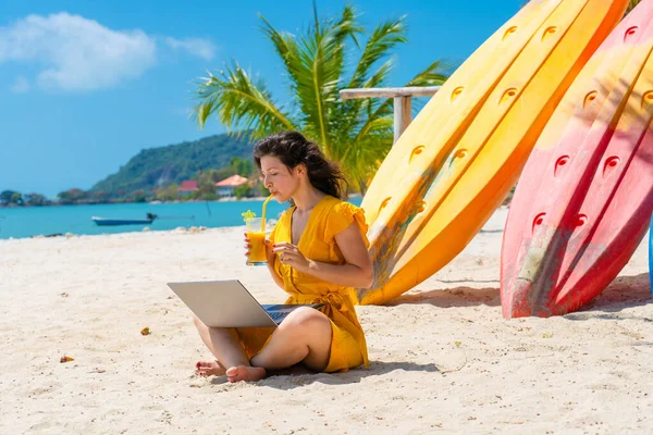 Дівчина Жовтій Сукні Тропічному Піщаному Пляжі Працює Ноутбуці Поблизу Каяків — стокове фото