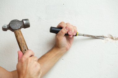 Binanın tamiri. Bir adam duvara kablo döşemek için hendek kazar. Duvara elektrik kabloları döşeniyor.