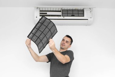 Adam evdeki klimanın filtresini tozdan temizliyor. Adam çok kirli bir havalandırma filtresini ıslattı. Ve ellerinin arasında inceliyor. İklim ekipmanı bakımı